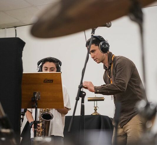 A boy playing the saxophone in a recording studio, with music leader