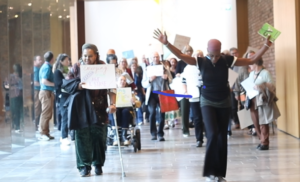 A parade of people in a corridor, holding their arms above their heads