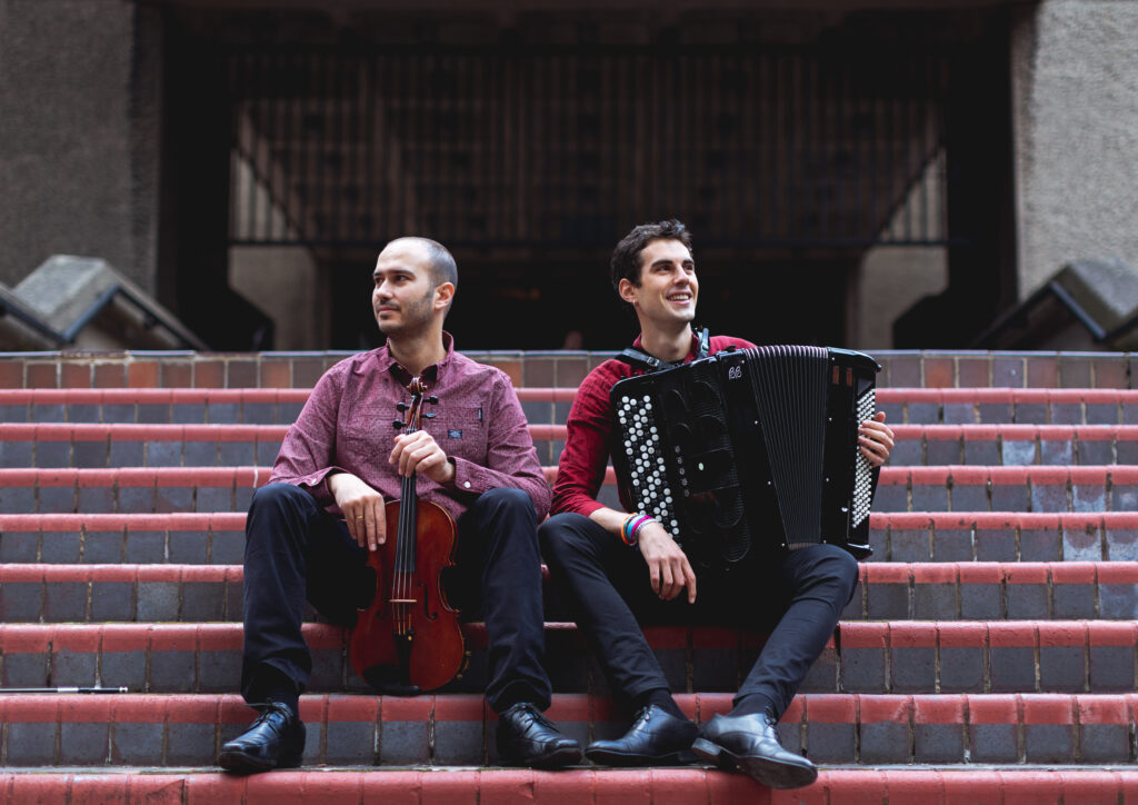 Two musicians sitting on some steps, holding a viola and an accordion.