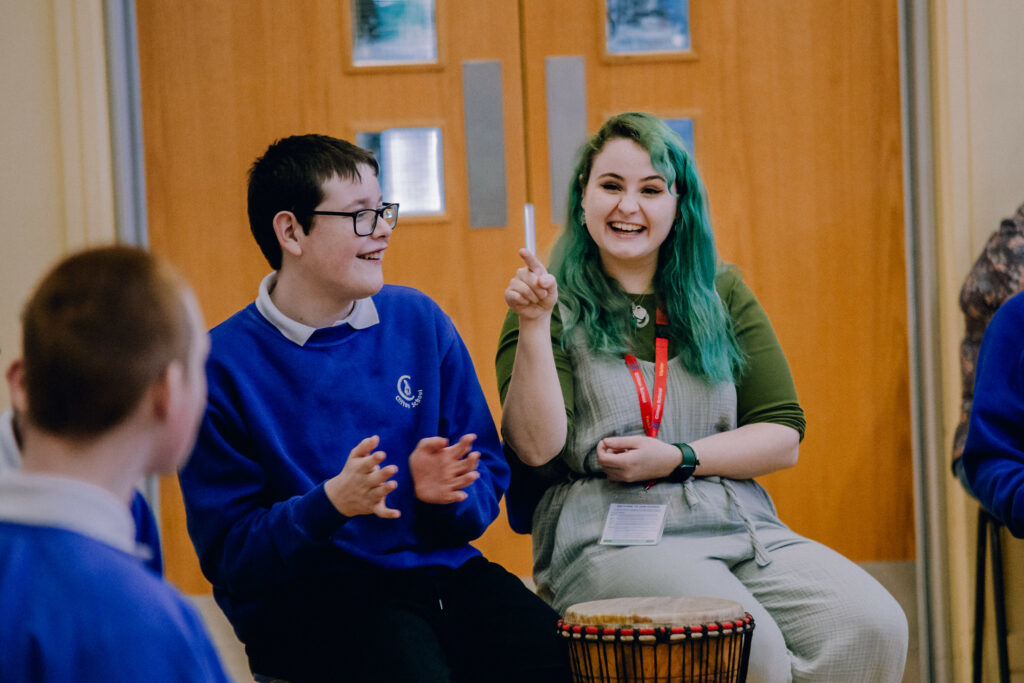 A musician sitting with school pupils during a workshop