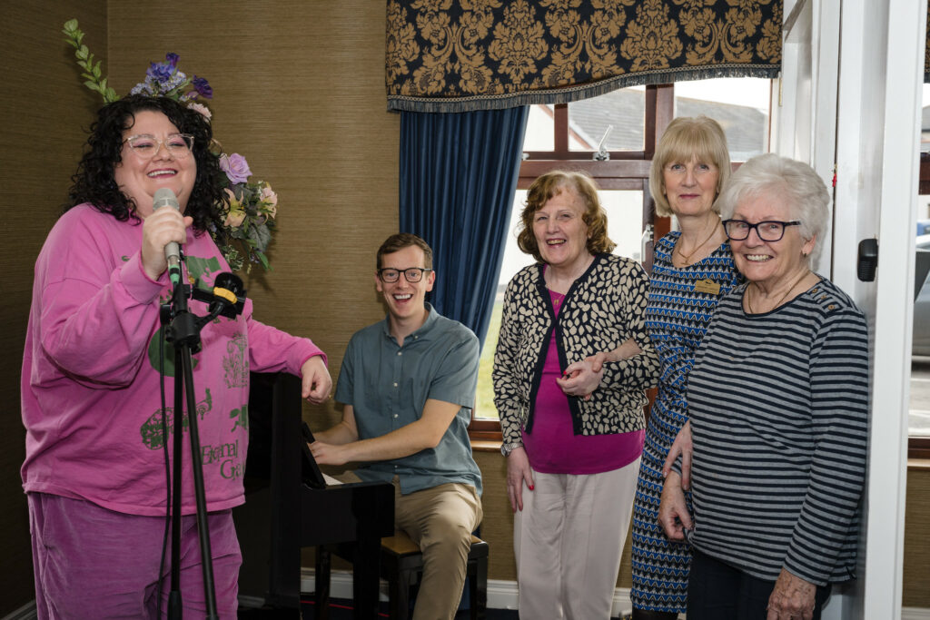 Musicians singing and playing piano with women at a care home
